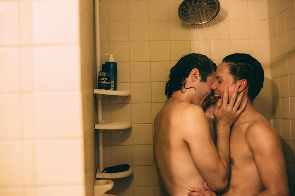 Dos personas en la ducha, sonriendo y tocándose la cara con las manos.