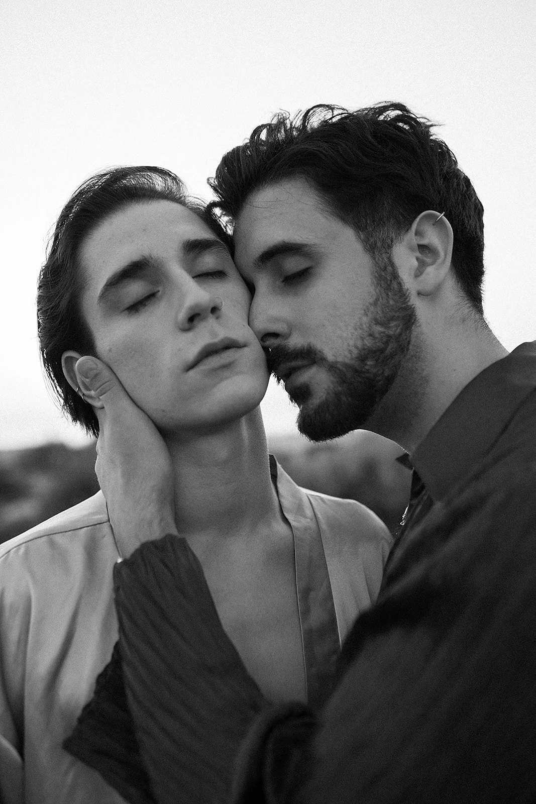 Dos personas, un hombre y una mujer, con los ojos cerrados, en una pose íntima, tocándose la cara con las manos en un ambiente natural, en blanco y negro.