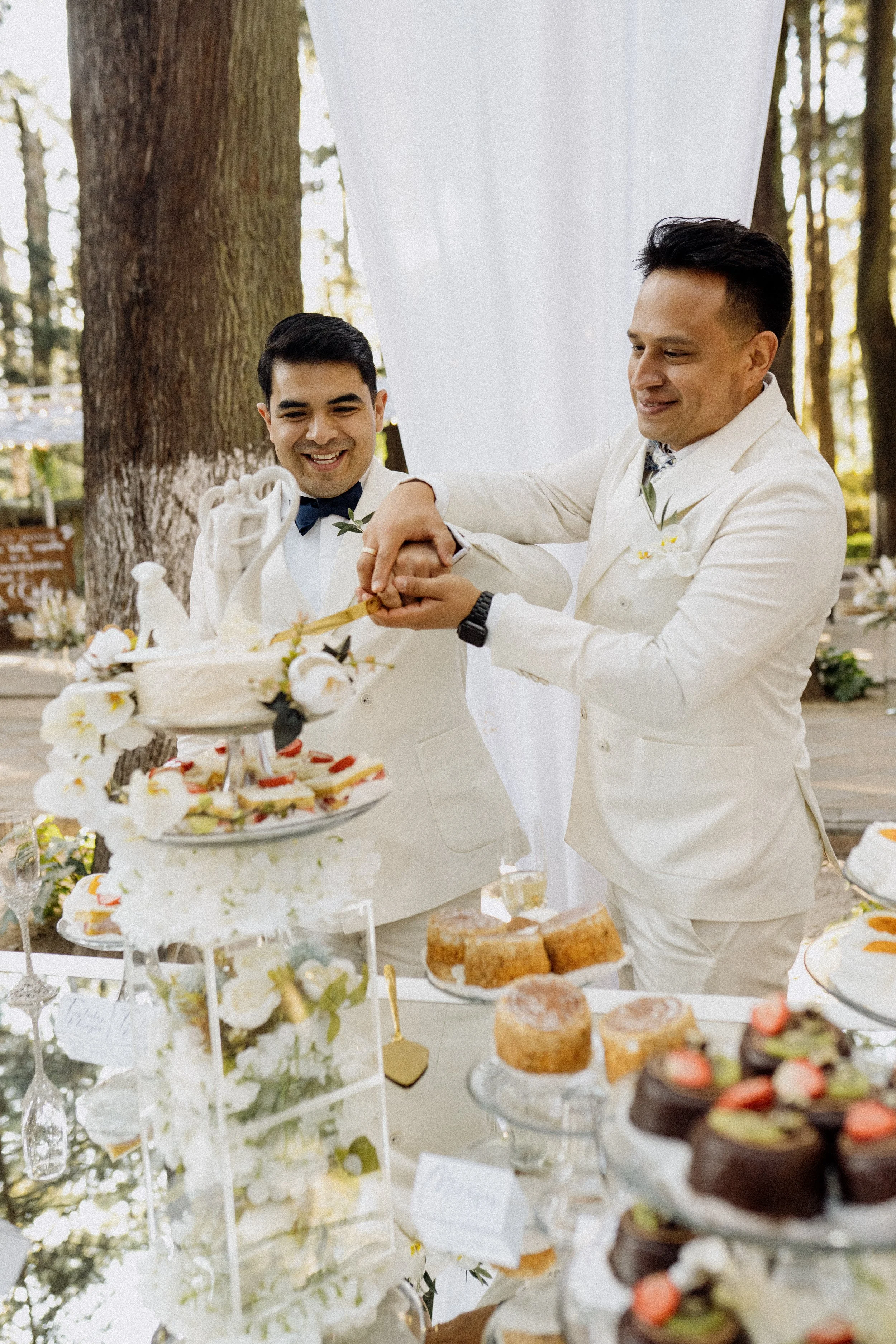 Pareja de hombres en boda cortando un pastel en un evento al aire libre
