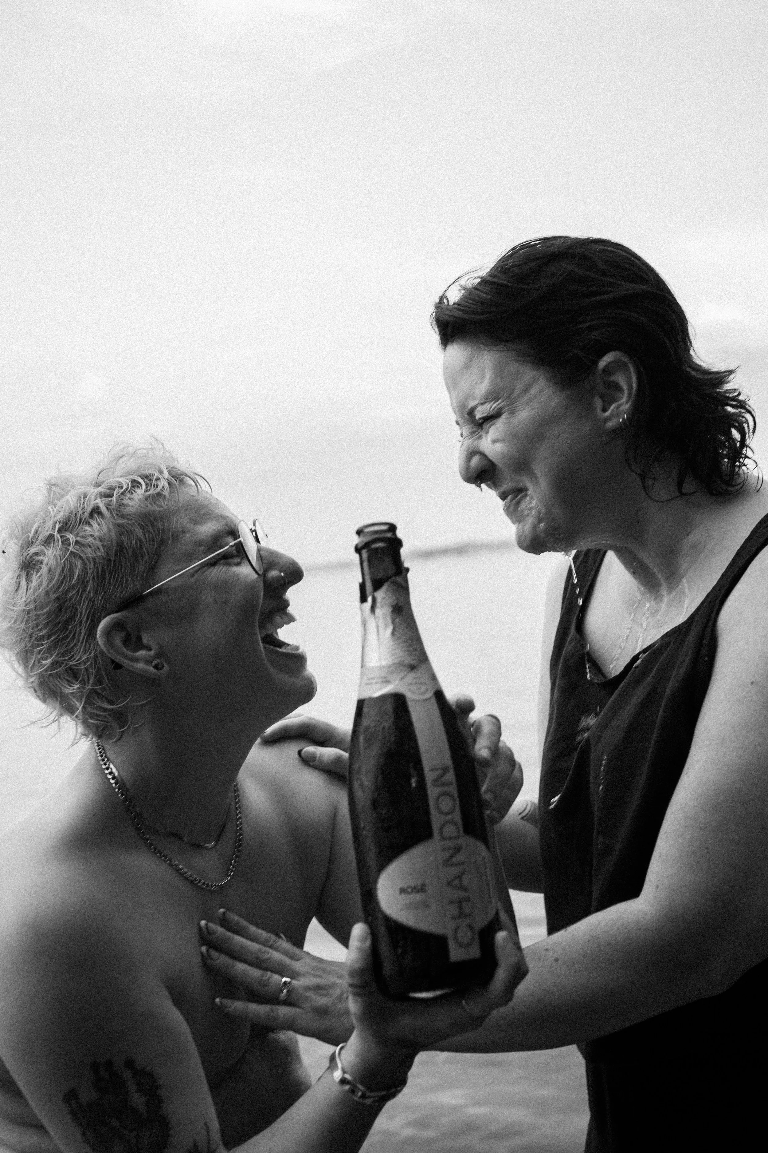 Dos personas riendo y bebiendo cervezas en la playa, en un entorno relajado y feliz.