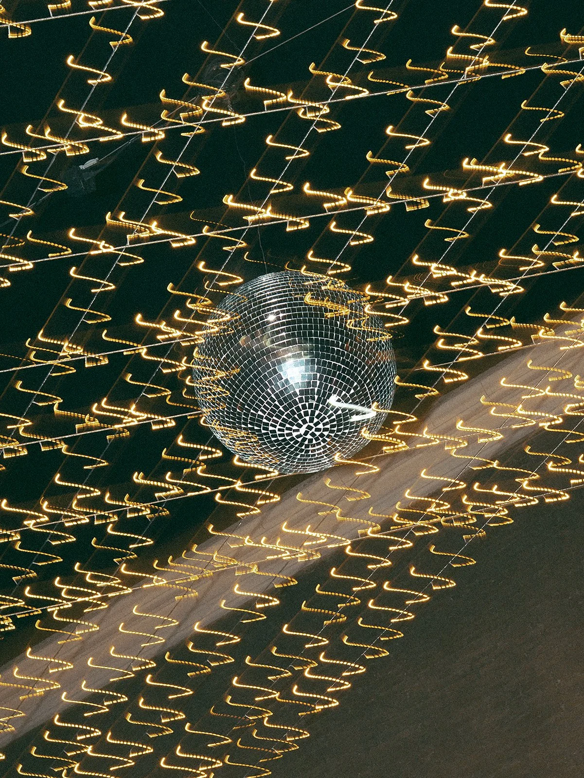 Esfera de espejos suspendida con luces amarillas parpadeantes en un fondo oscuro, creando un efecto de movimiento y distorsión.
