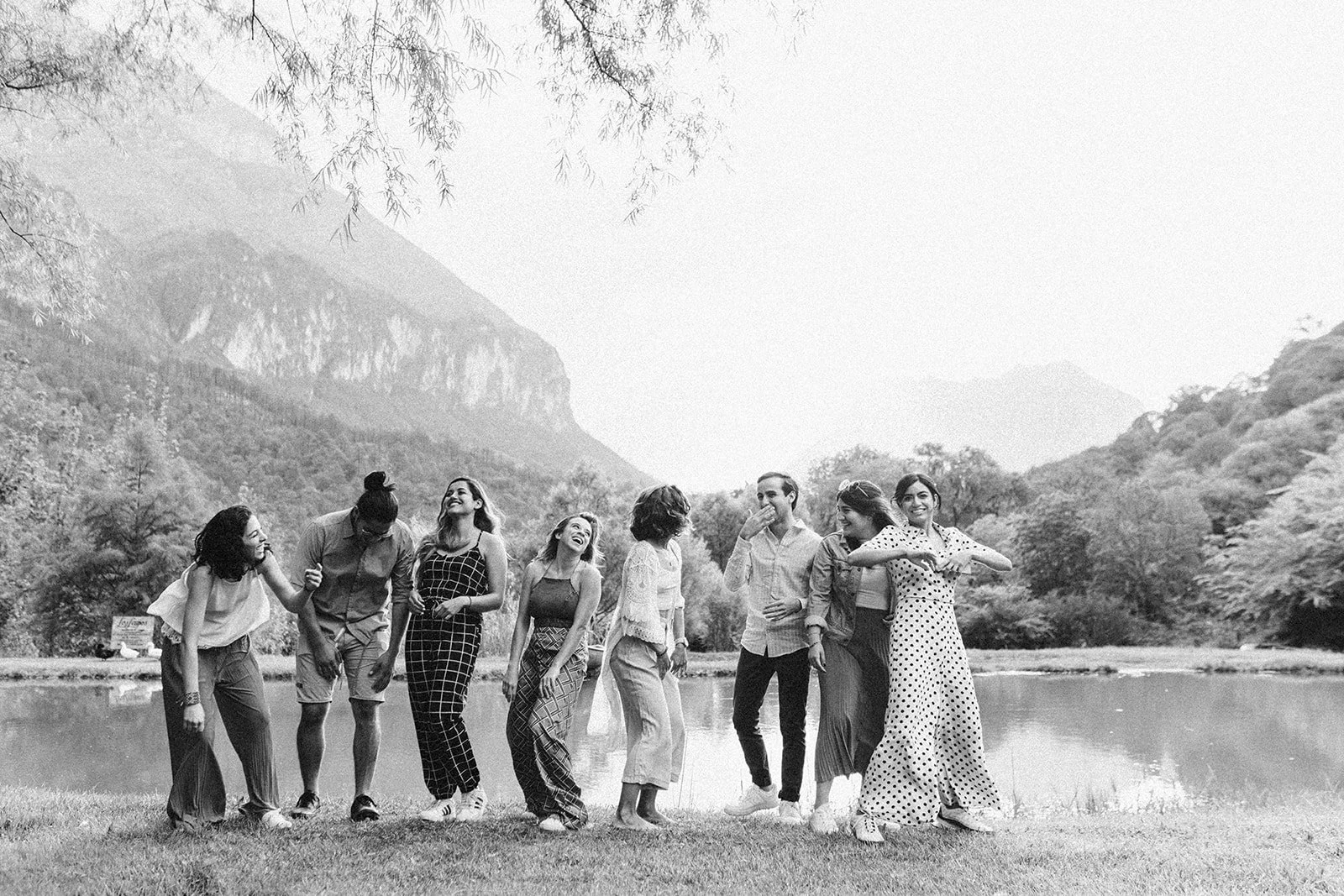 Grupo de ocho personas, mujeres y hombres, en la orilla de un lago rodeado de montañas, caminando y riendo, en un entorno natural