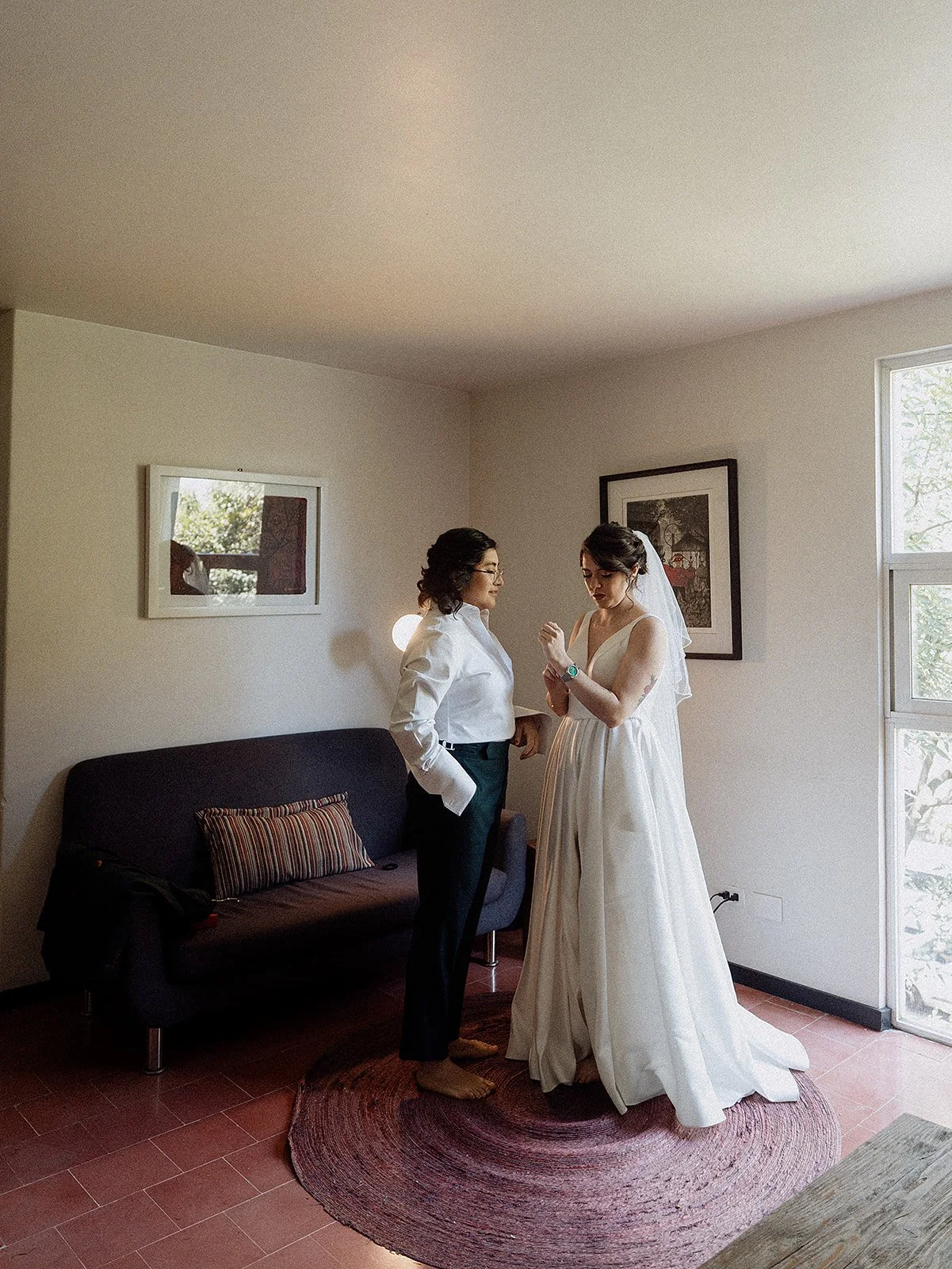 Mujer vestida de novia en una habitación, siendo ayudada por otra mujer, posiblemente en preparación para su boda.