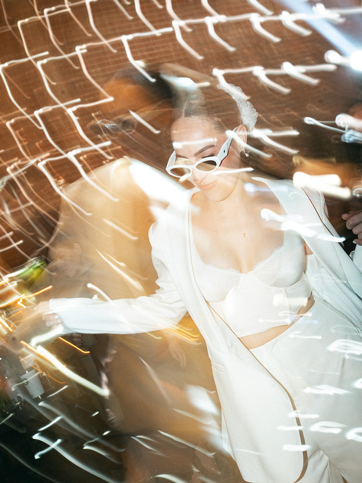 Mujer con gafas blancas y ropa blanca en medio de luces brillantes en movimiento.