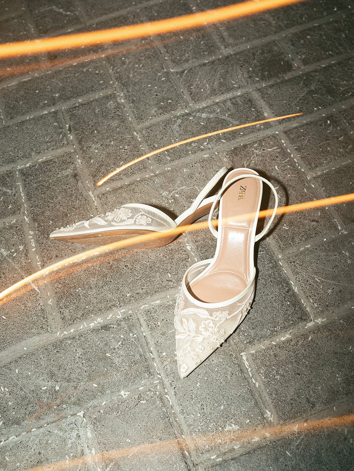 Zapatos de tacón altos de encaje con bordados florales, vistos desde arriba, en un piso de ladrillos grises.