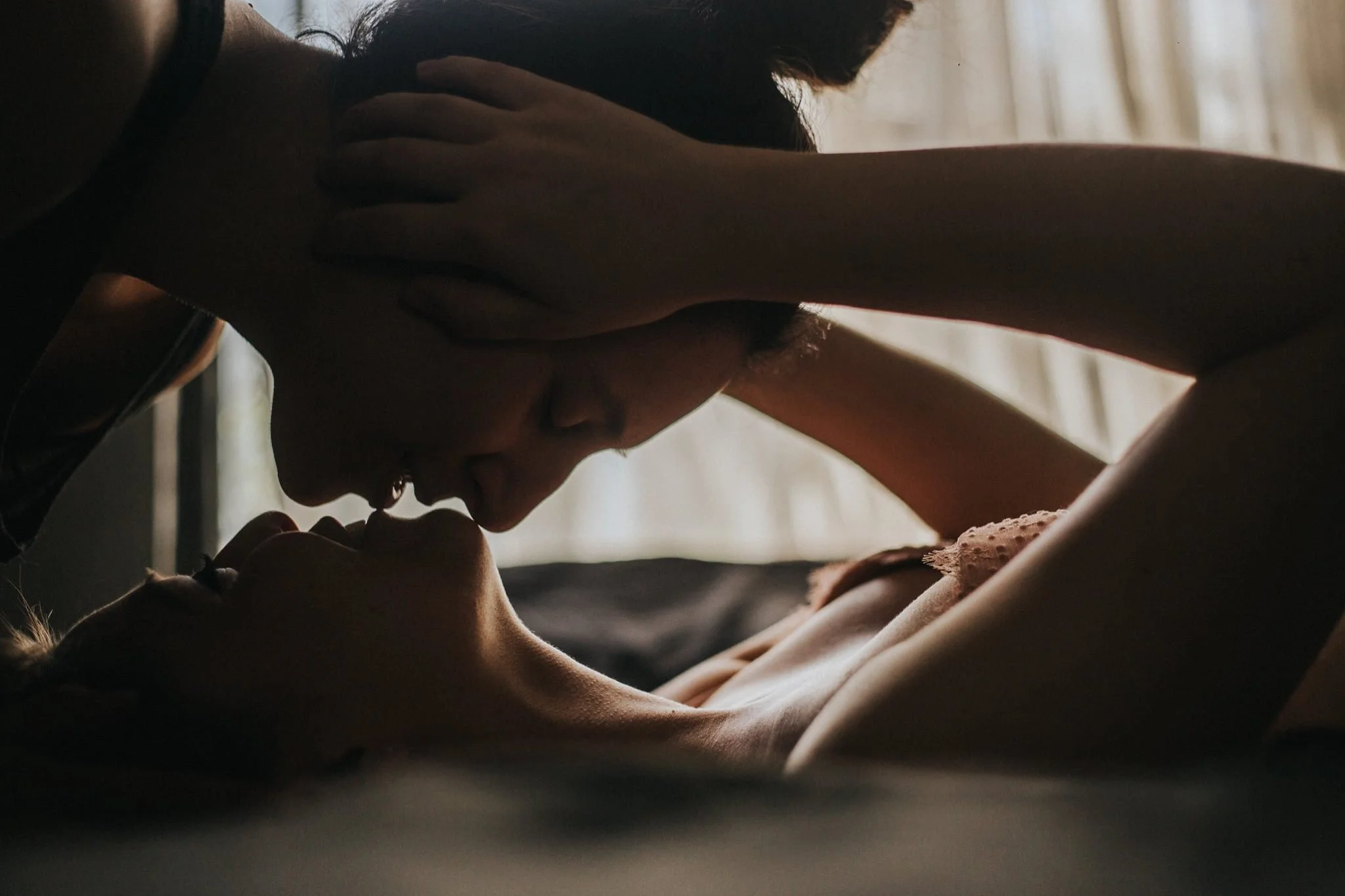 Una pareja en una escena íntima, uno de ellos acariciando la cara del otro en un ambiente con poca luz.