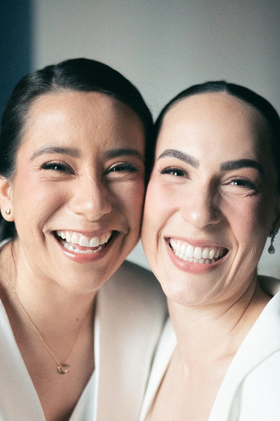Dos mujeres sonriendo juntas, en primer plano, en un ambiente interior.