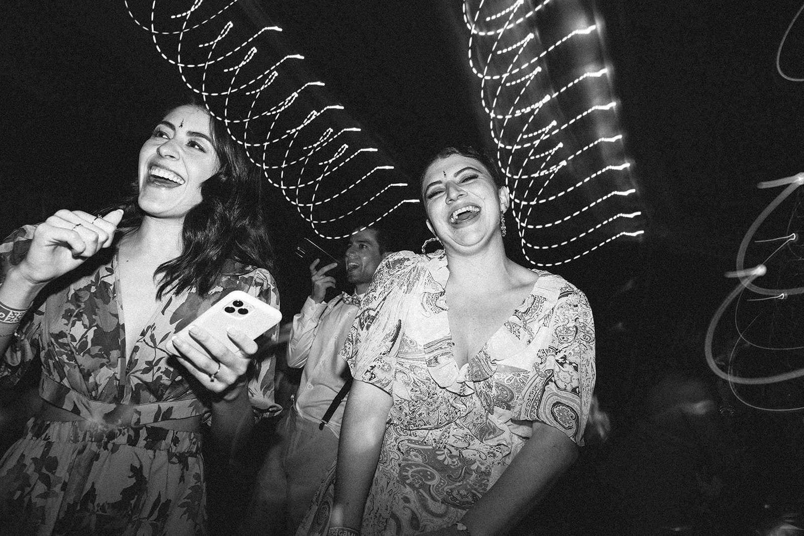 Grupo de personas sonriendo y riendo en un evento, con luces en el fondo en un ambiente oscuro.