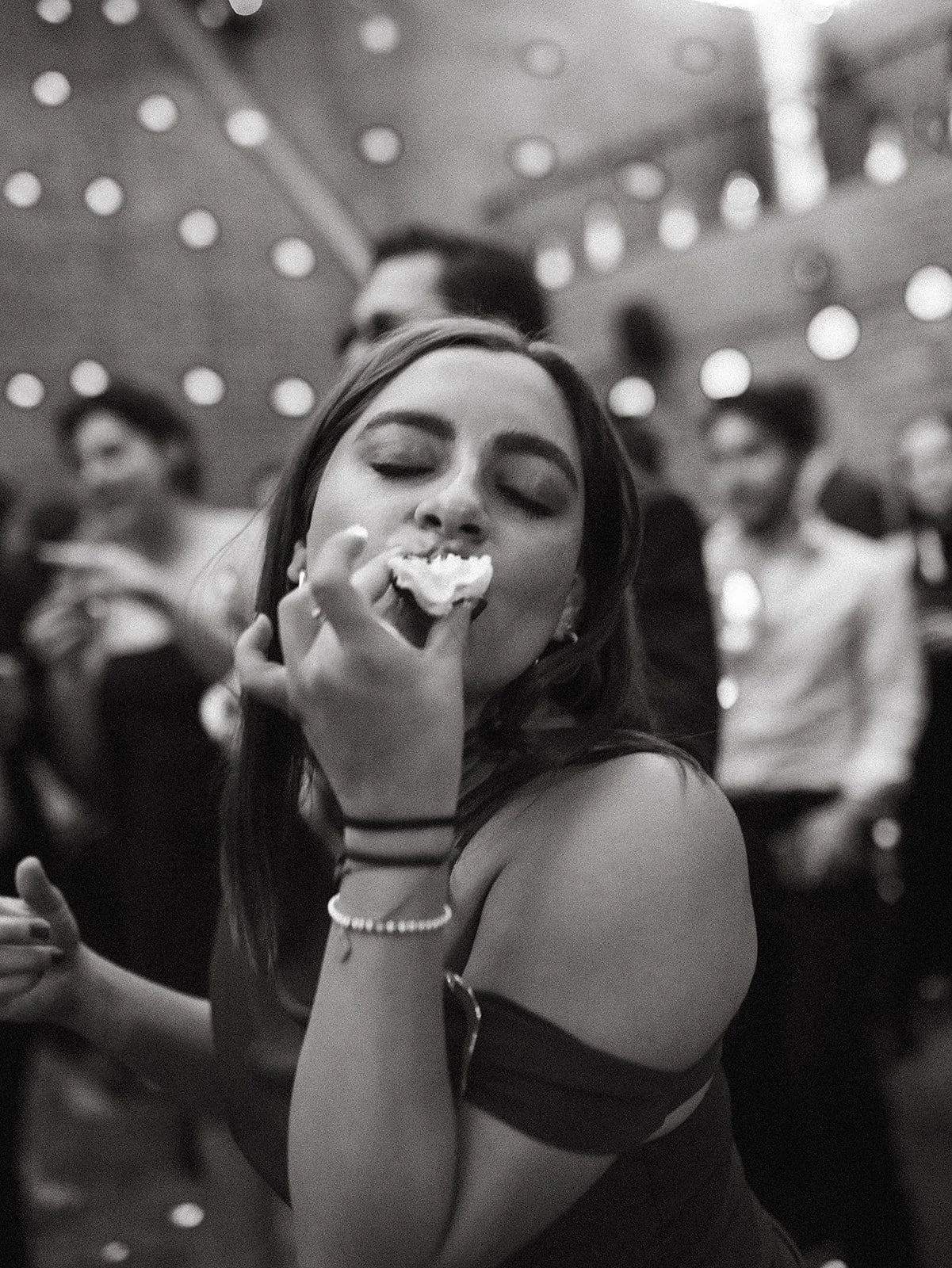 Joven mujer comiendo pastel en una fiesta con varias personas en el fondo.