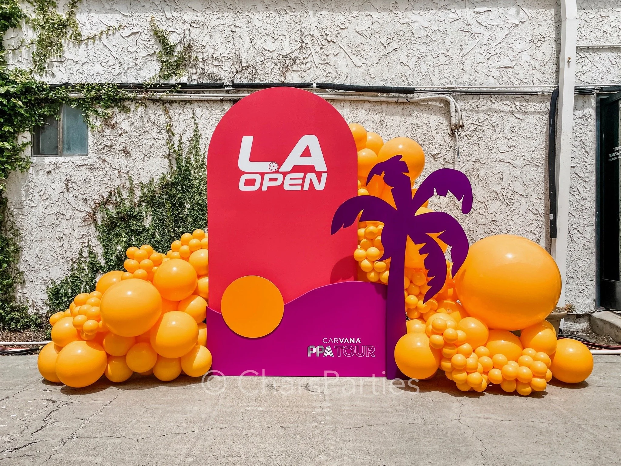 Colorful LA Open sign with orange balloons, custom backdrop, and a palm tree decoration