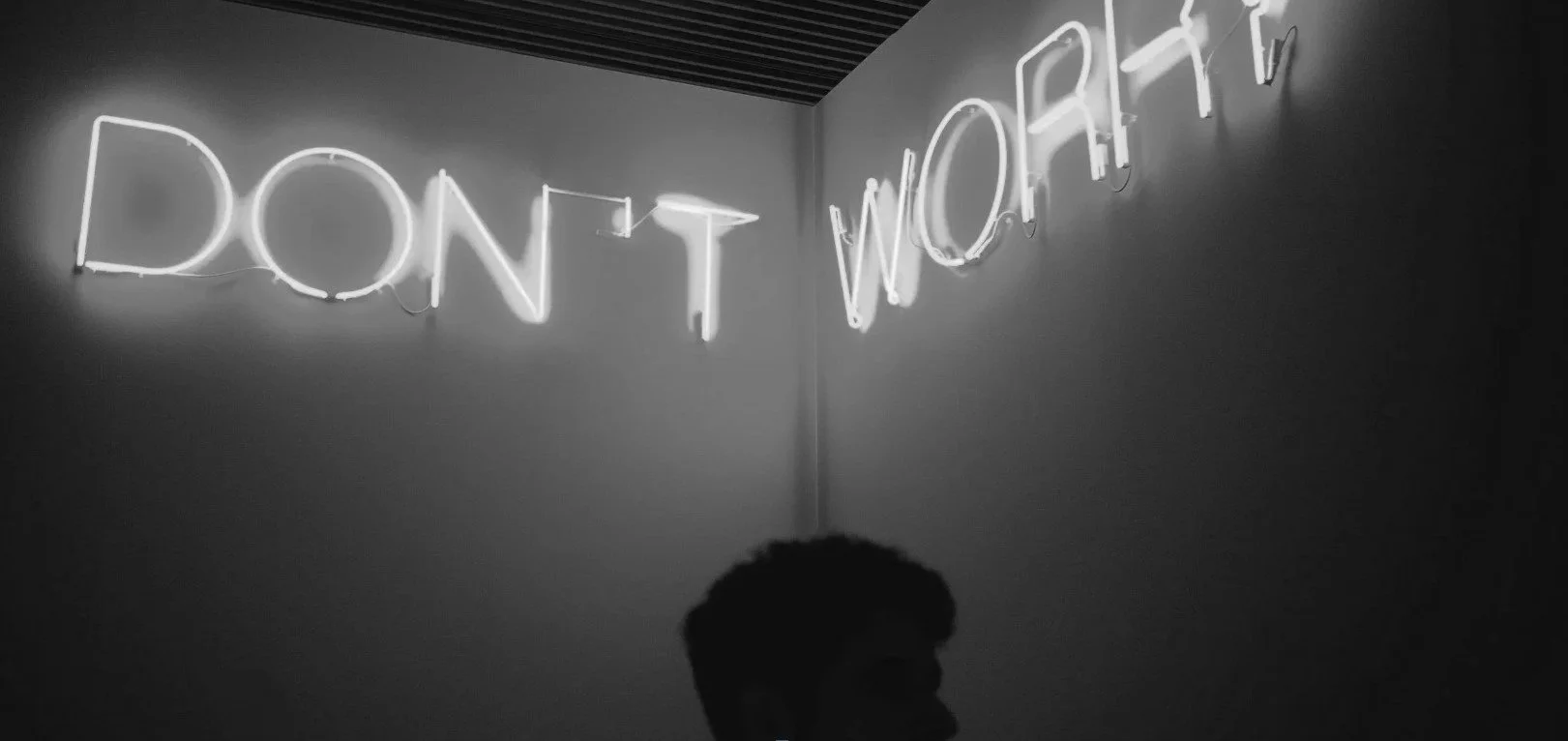 Neon sign on a wall reading "DON'T WORRY" in white with a person silhouette below