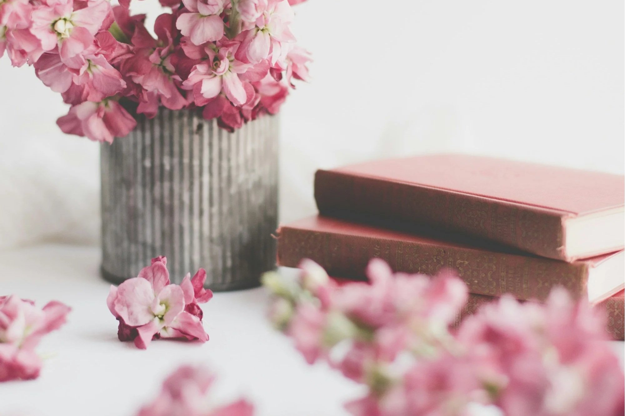 Pink flowers in a striped vase with closed pink books beside it, on a white surface.