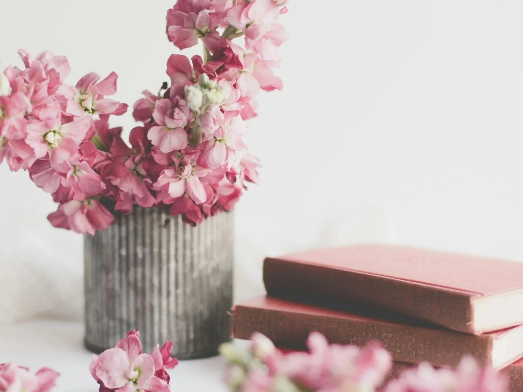 Pink flowers in a striped gray and white vase, with two closed pink chocolate boxes on the right side, on a white content writer's against a plain white background.