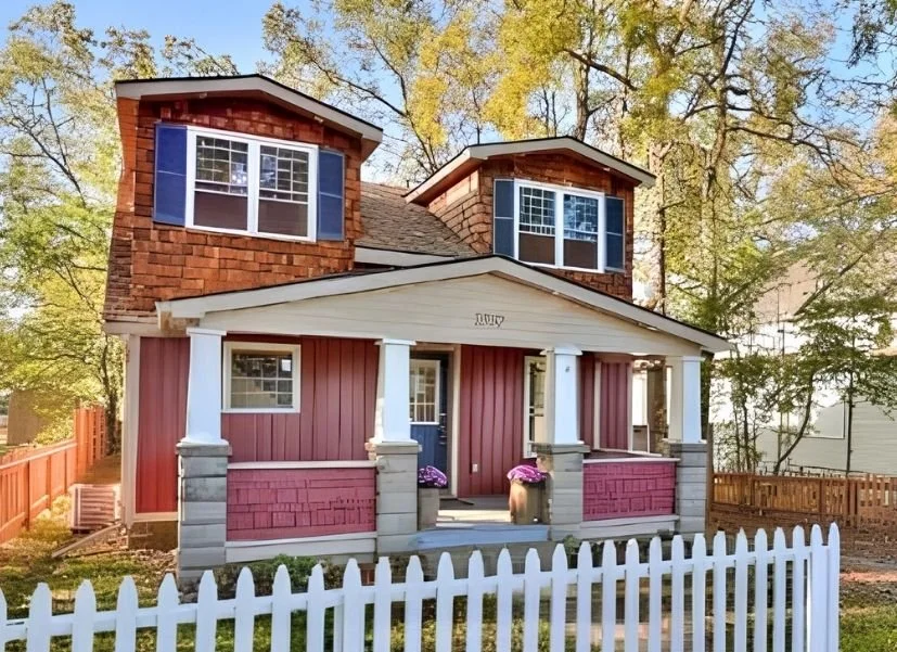 Colorful two-story house with red and blue exterior, white picket fence, surrounded by trees.