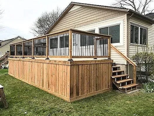 Wooden deck with railing attached to the back of a house, with stairs leading up to the deck and a grassy yard surrounding it.