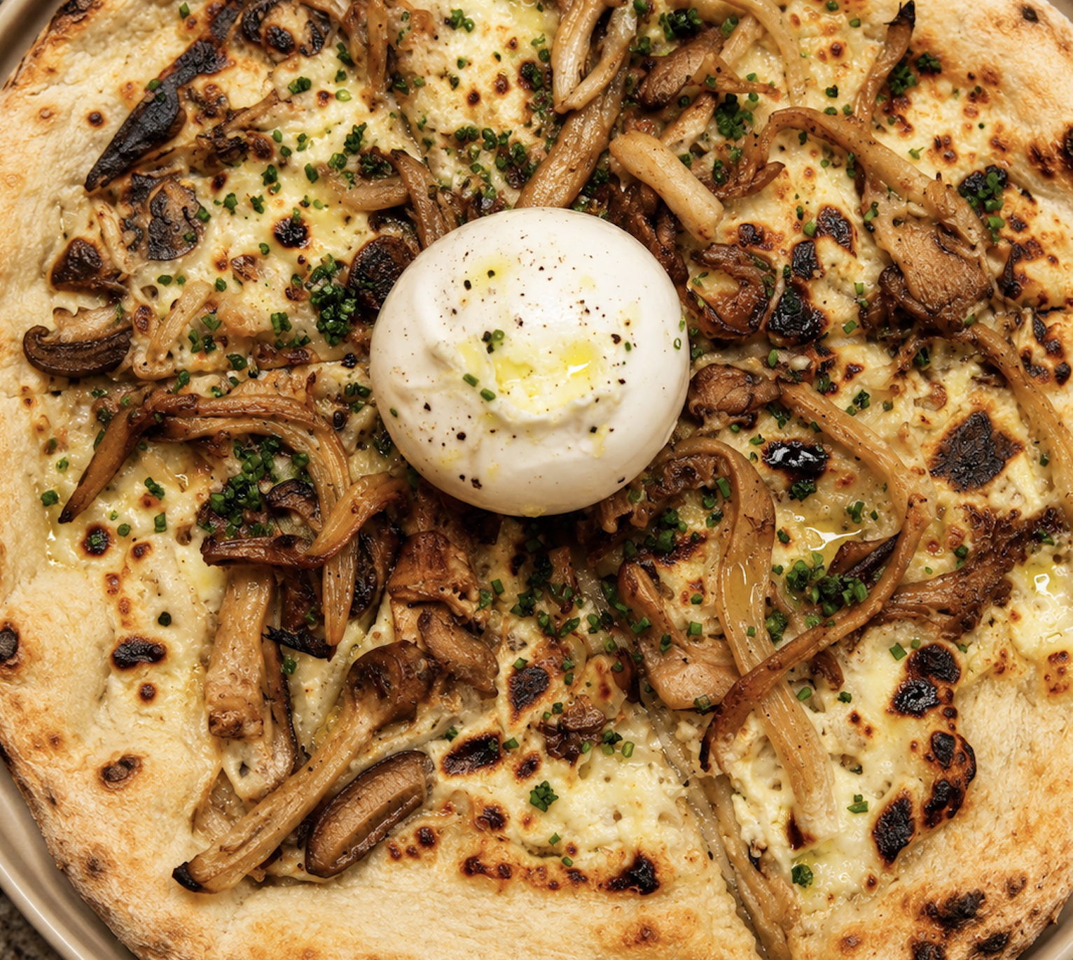 Pizza with sautéed mushrooms, chopped chives, and a poached egg in the center, with a golden crust.