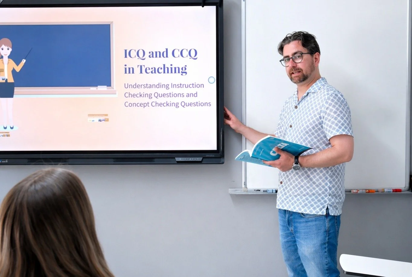 A male teacher with glasses and a beard holding a book, standing at the front of a classroom near a digital screen, giving a presentation titled 'ICO and CCQ in Teaching'.