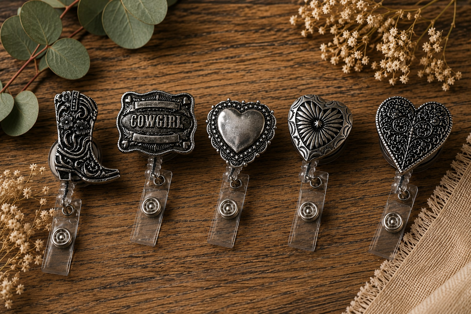 Set of five decorative badge clips on a wooden surface, surrounded by greenery and small flowers.