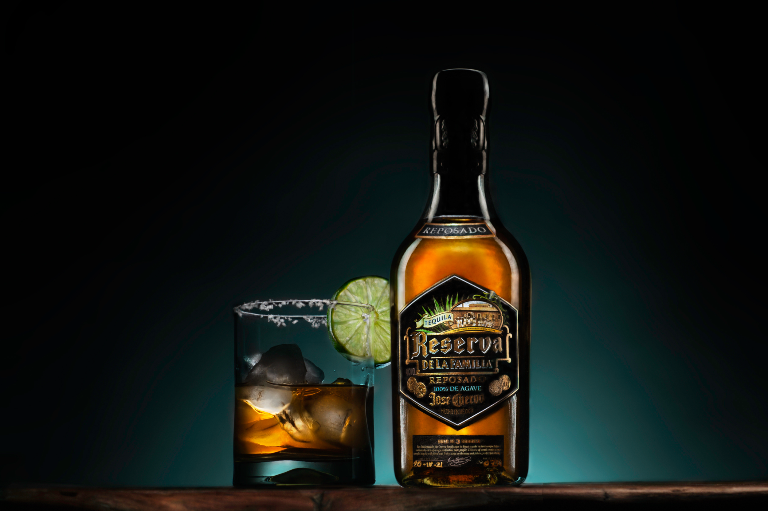 A bottle of Jose Cuervo Reserva de la Familia Reposado tequila with a lime slice and a glass with ice and lime, set against a dark background.