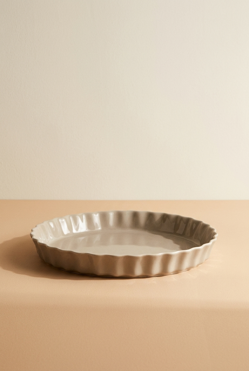 Plate en céramique beige avec une bordure rainurée, posé sur une surface beige claire.
