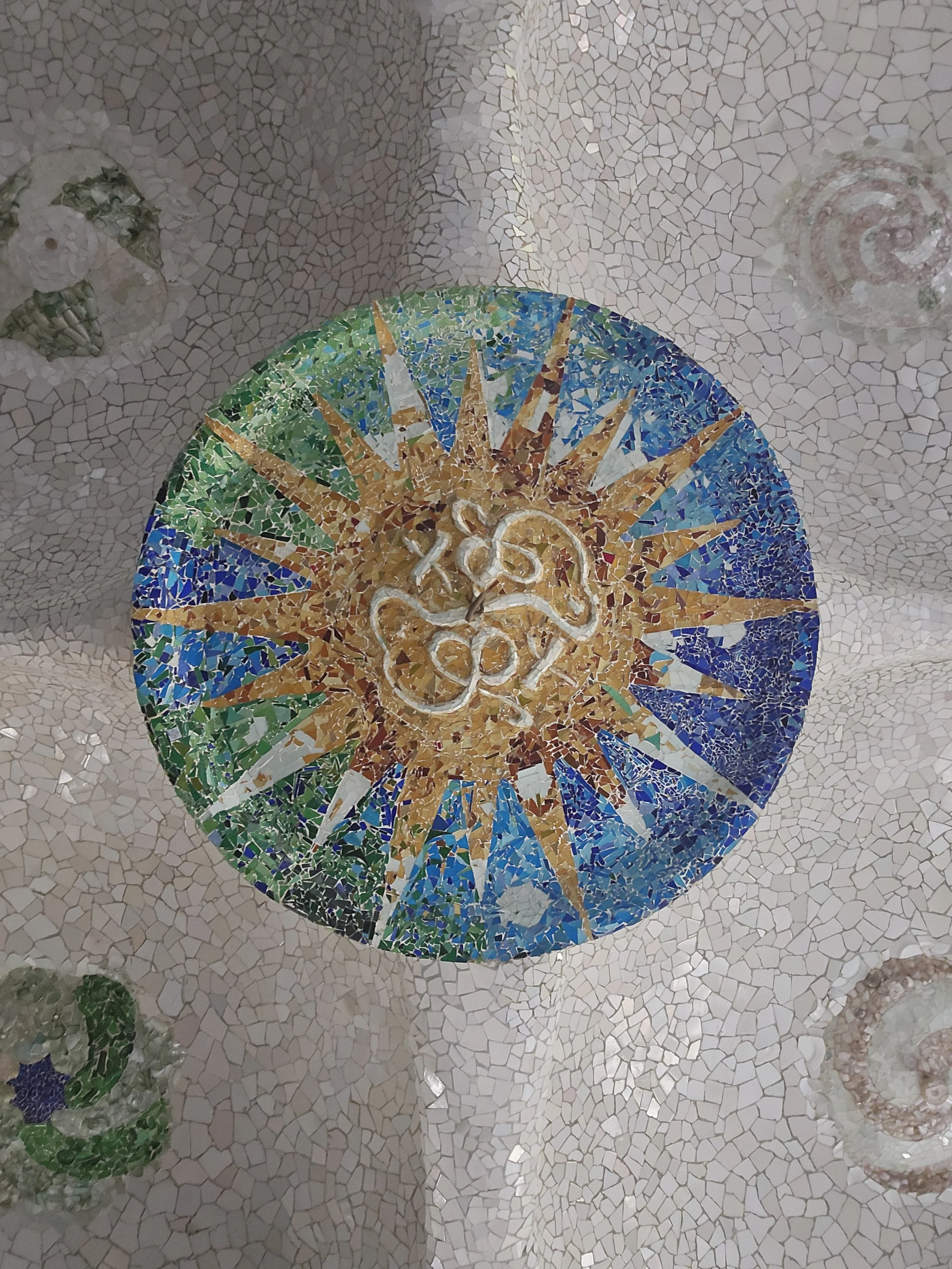 Barcelona, Spain - Colorful mosaic clock with a background of beige mosaic tiles and decorative green and pink mosaic elements.