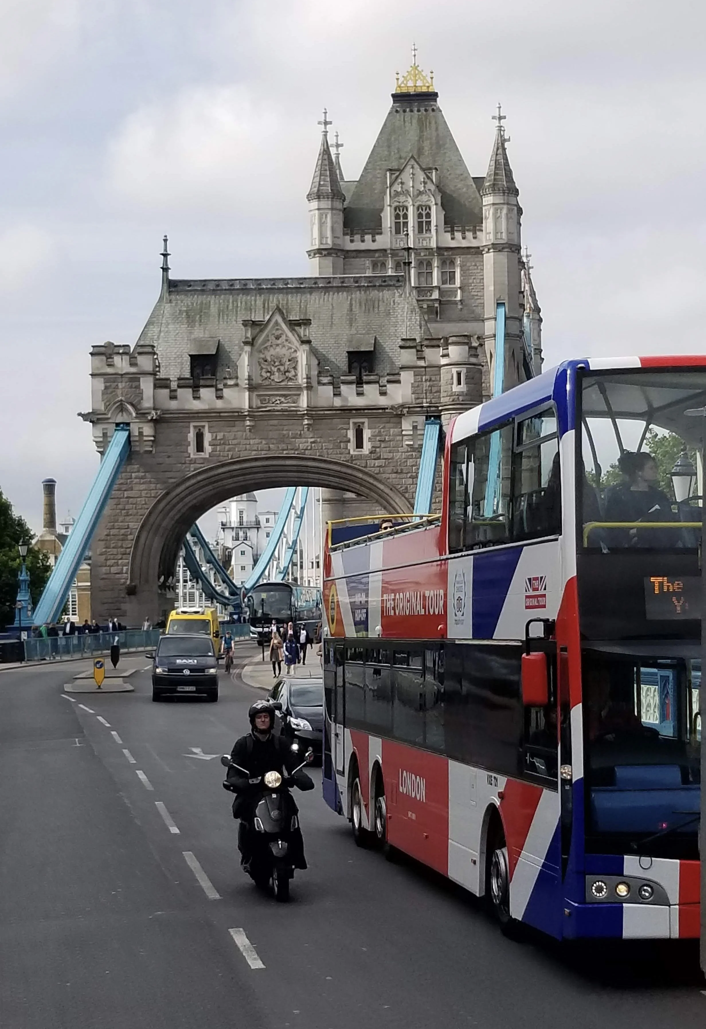 Tower Bridge in London with a double-decker tour bus, cars, and a motorcyclist on the street.
