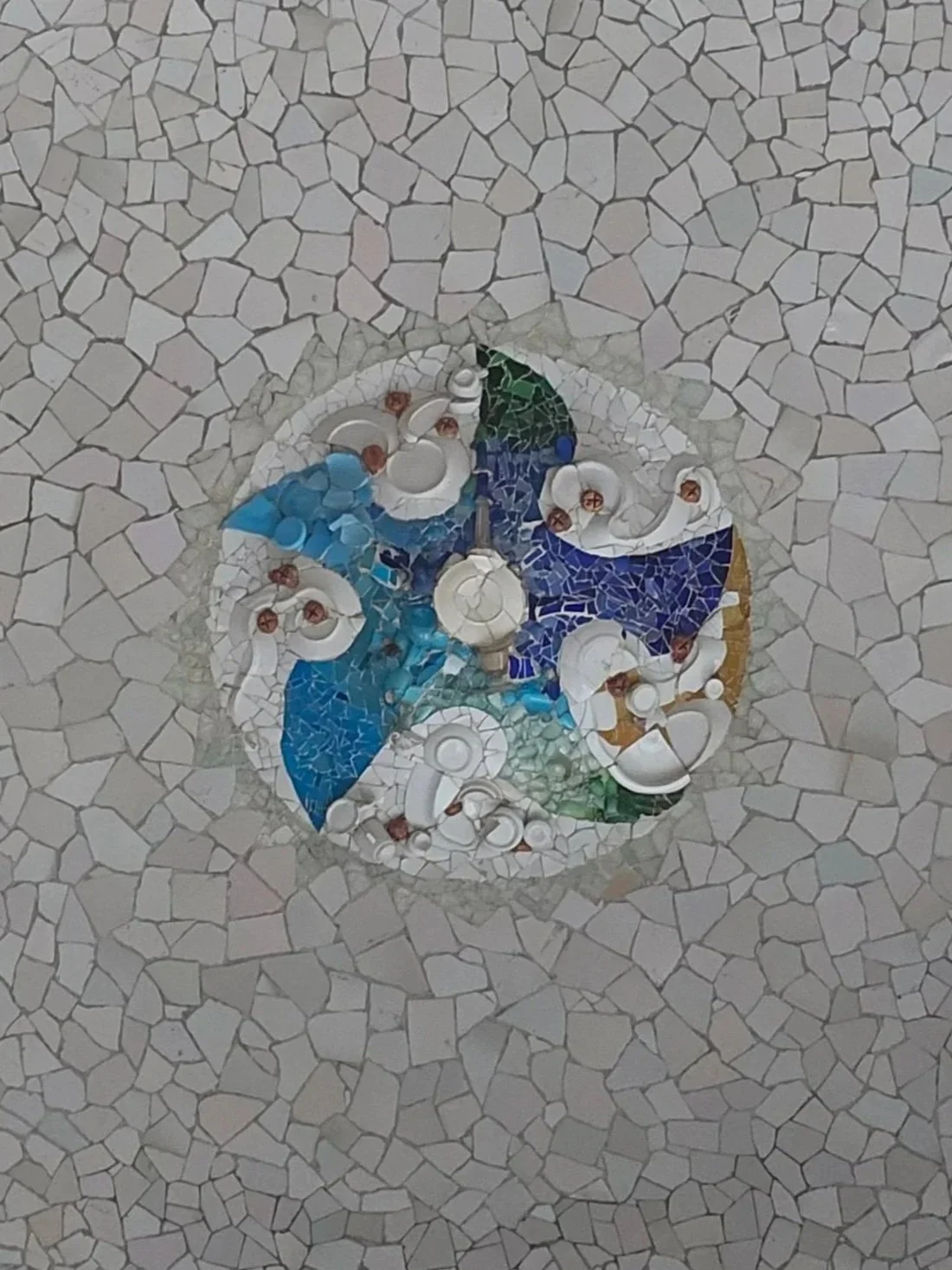 A circular mosaic embedded in a tiled floor, featuring images of lamps and colors like blue, green, and yellow.