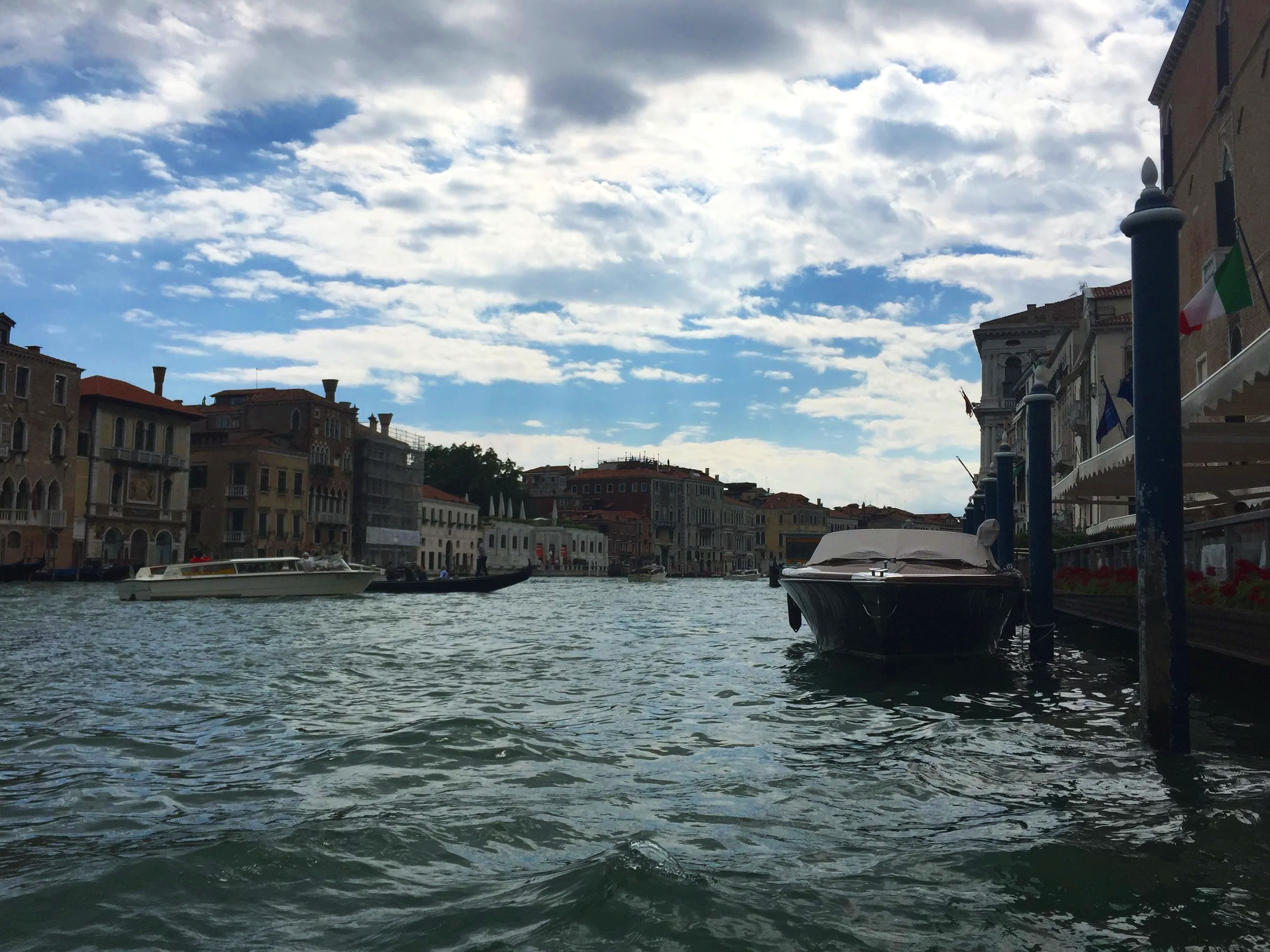 View of a canal with boats, surrounded by colorful buildings under cloudy sky, possibly Venice.