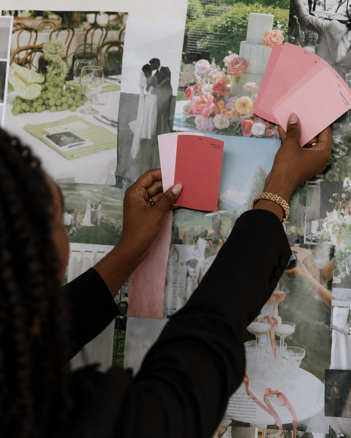 A woman with dark skin and braided hair looking at a collage of wedding photos and color swatches, holding pink fabric samples and a photograph of a wedding cake with pink flowers.