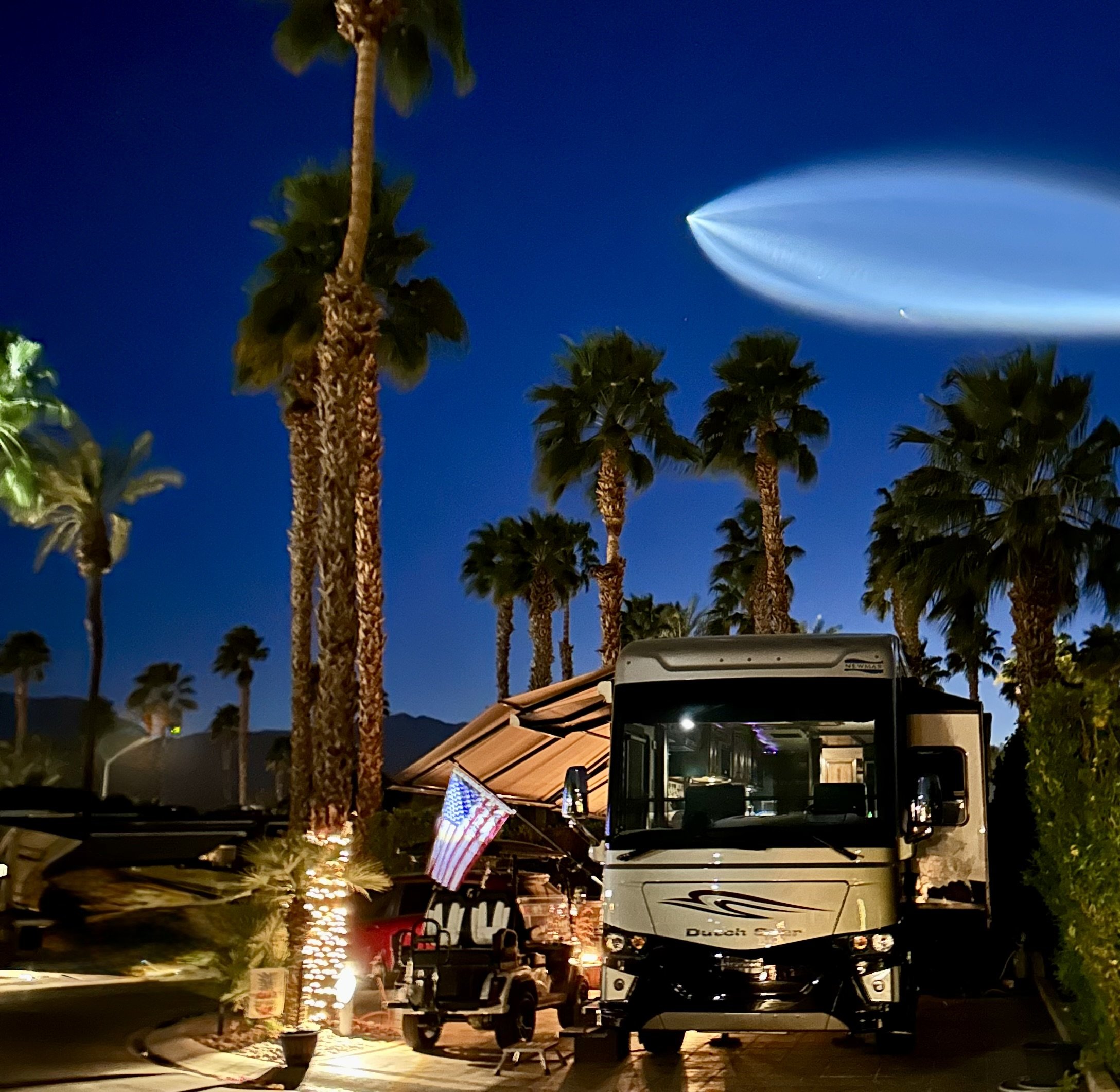 Luxury motorcoach resort at night with palm trees, illuminated landscaping and parked RVs.