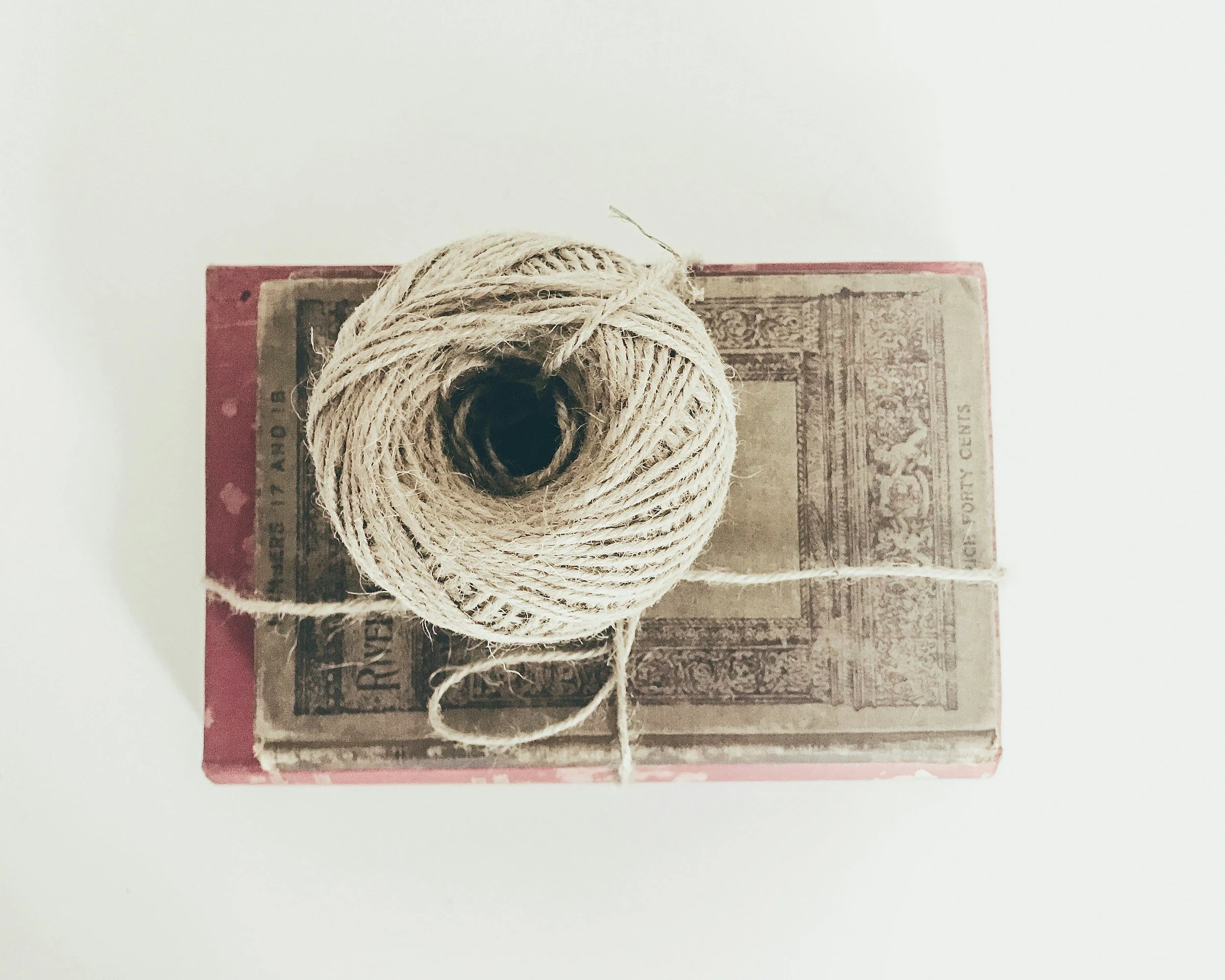 A ball of beige twine resting on an old, weathered dollar bill with a red border, on a white background.