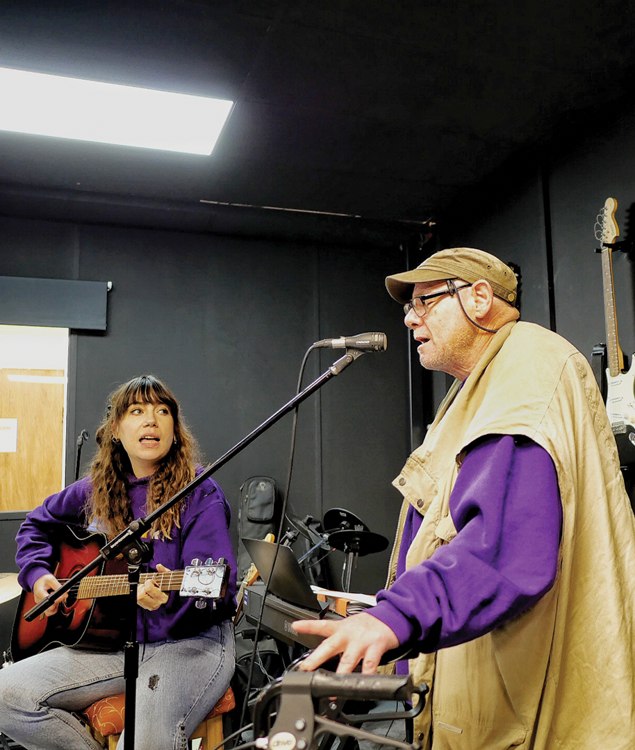 Key's music therapist plays guitar and accompanies a service user, a man with an acquired brain injury, who is singing in Key's black box studio.
