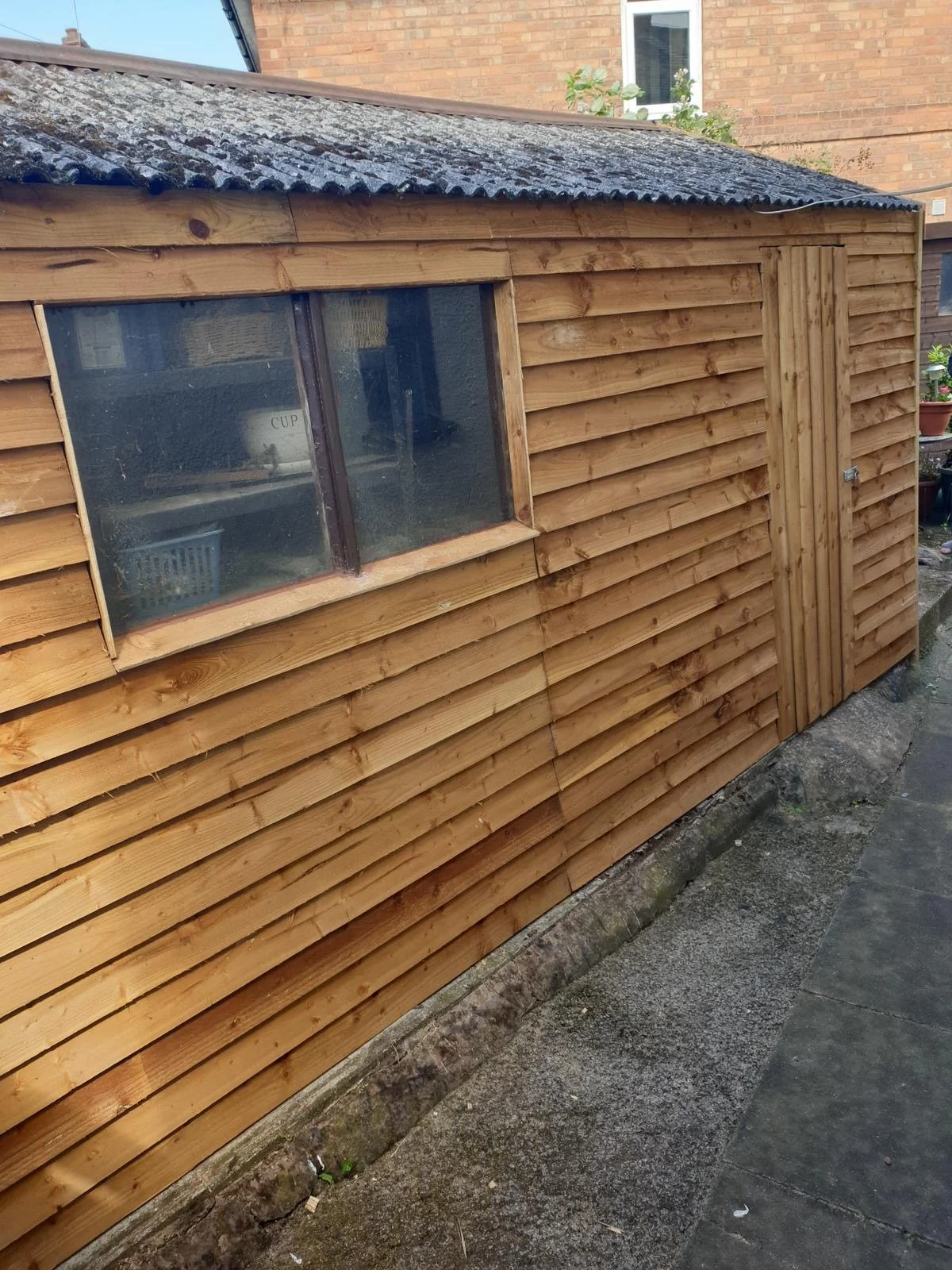 A newly built wooden garden shed with horizontal wooden planks, a small window, and a door