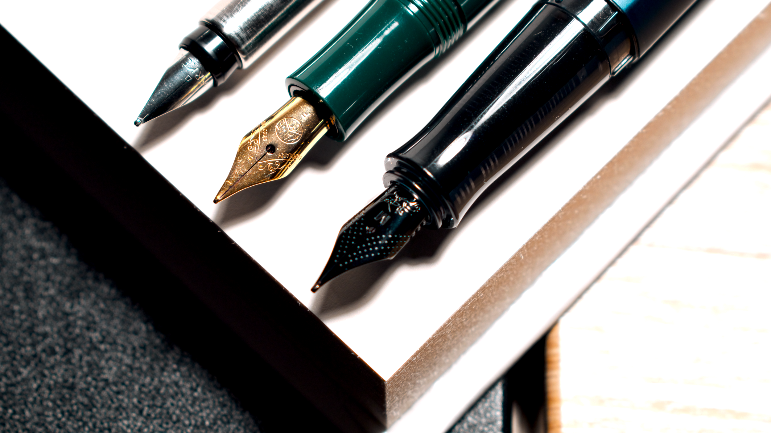 Close-up of three fountain pens with different nibs and body colors, placed on a surface.