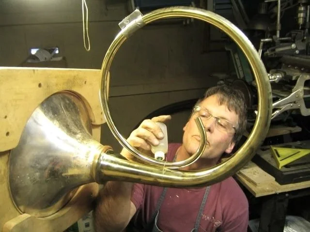 Bruce Roberts working on a large metal ring, part of a French horn, in a workshop.