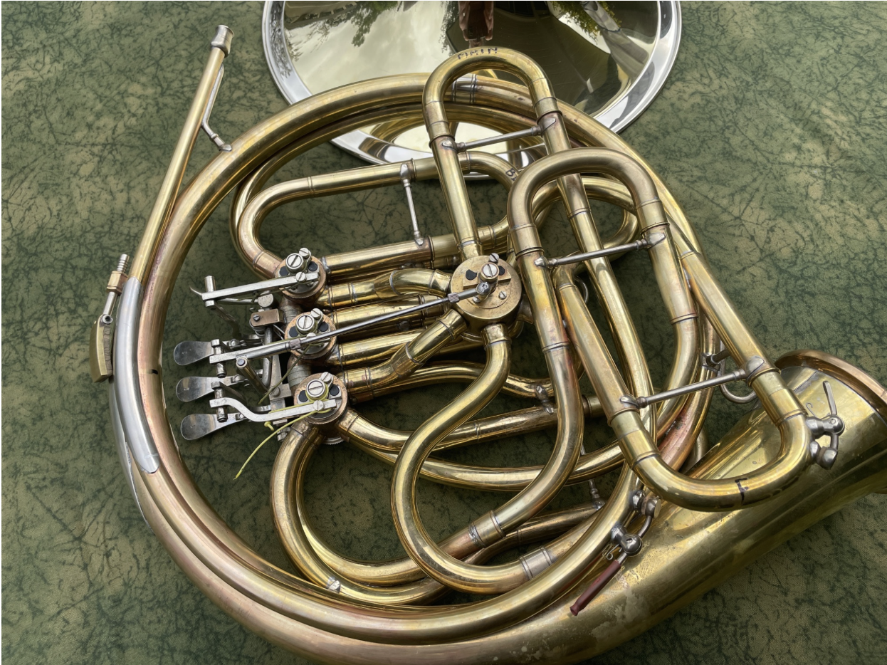 Close-up of a French horn with its tuning slides and valves, resting on a green textured surface with the bell in the background