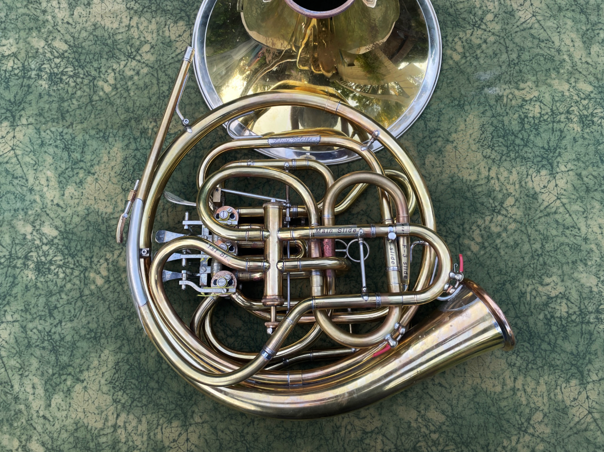 A brass French horn with a bell facing upward on a textured green surface.
