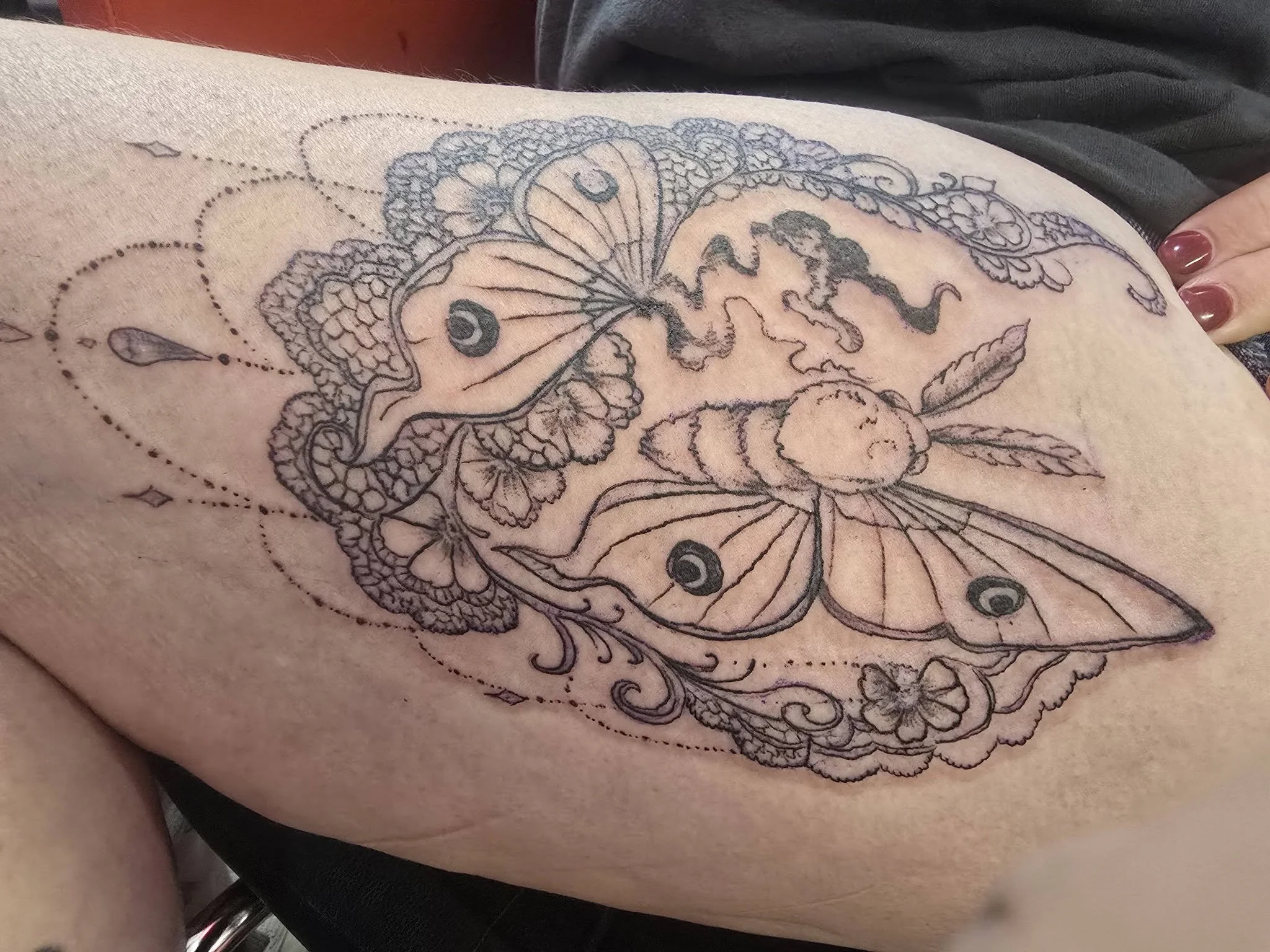 A detailed tattoo of a butterfly with floral and decorative elements on a person's skin.