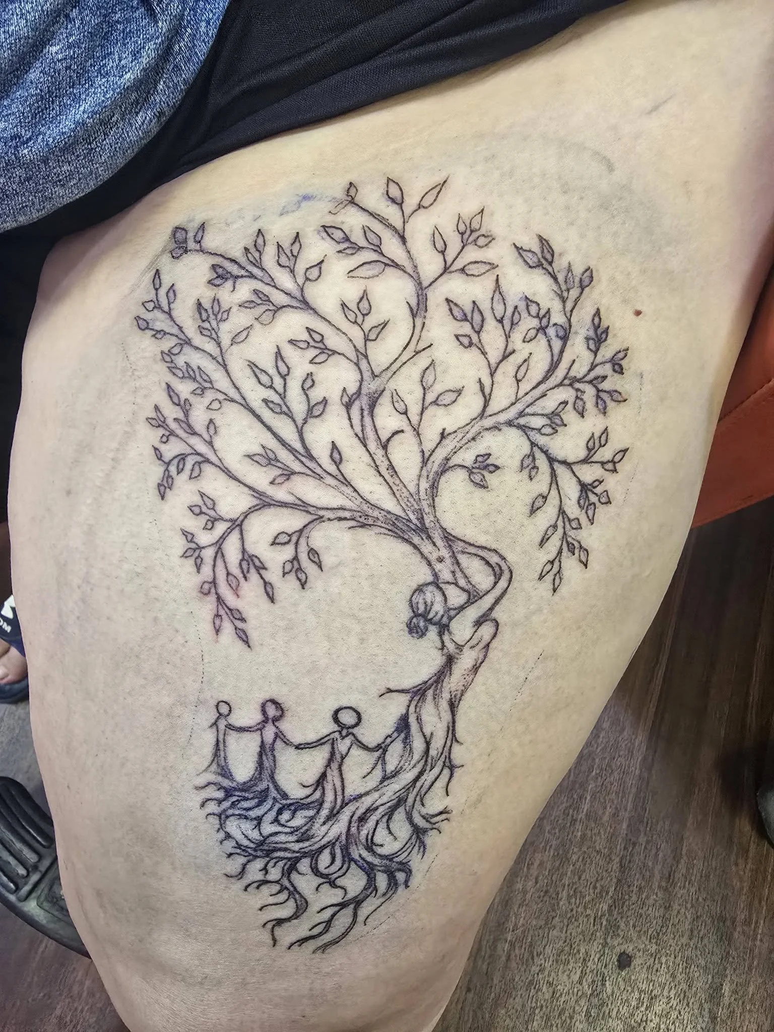 Tattoo design of a tree with interconnected branches and roots, with three stick-figure people holding hands at the bottom.