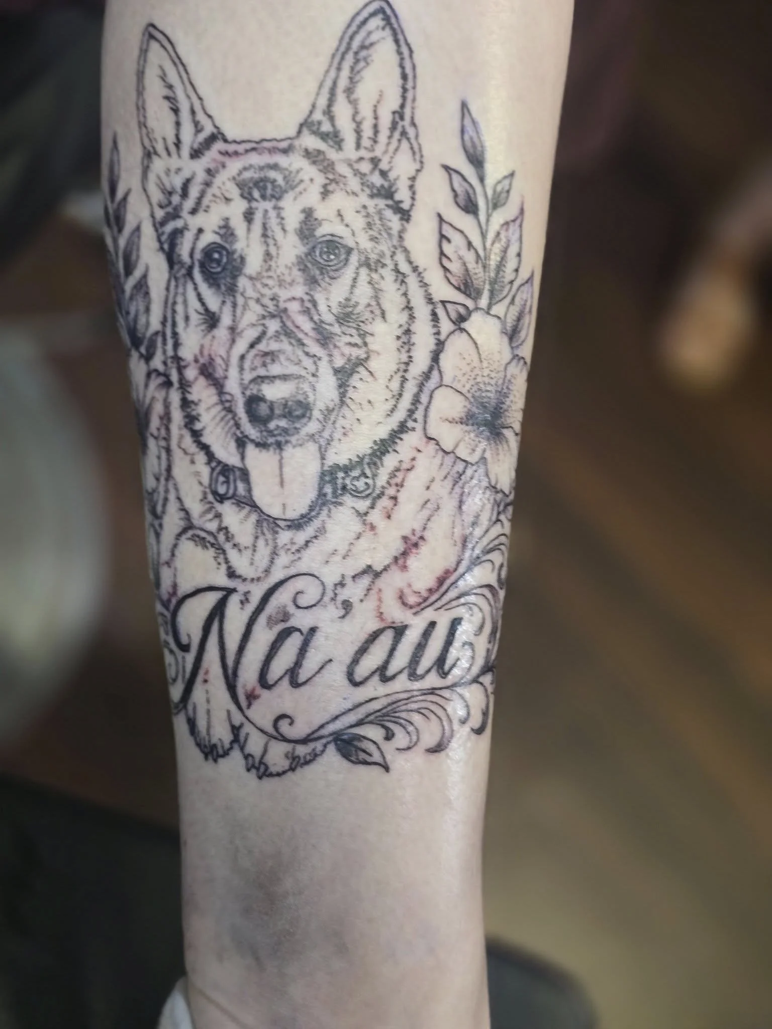 Tattoo of a dog's face with pointed ears and a flower, with decorative script text below.