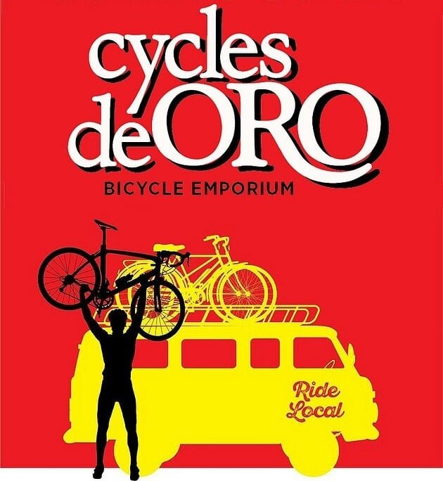 Red background with white and black text reading 'Cycles de Oro Bicycle Emporium Ride Local'. Silhouette of a person holding two yellow bikes and standing in front of a yellow van with bike racks on top, holding a black bike.