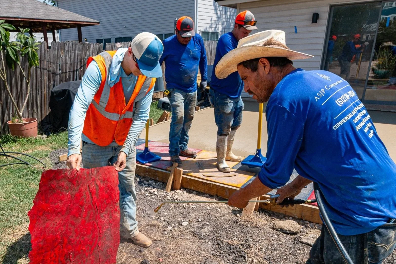 Group of construction workers pouring concrete for a sidewalk, with some holding tools and others preparing the area.