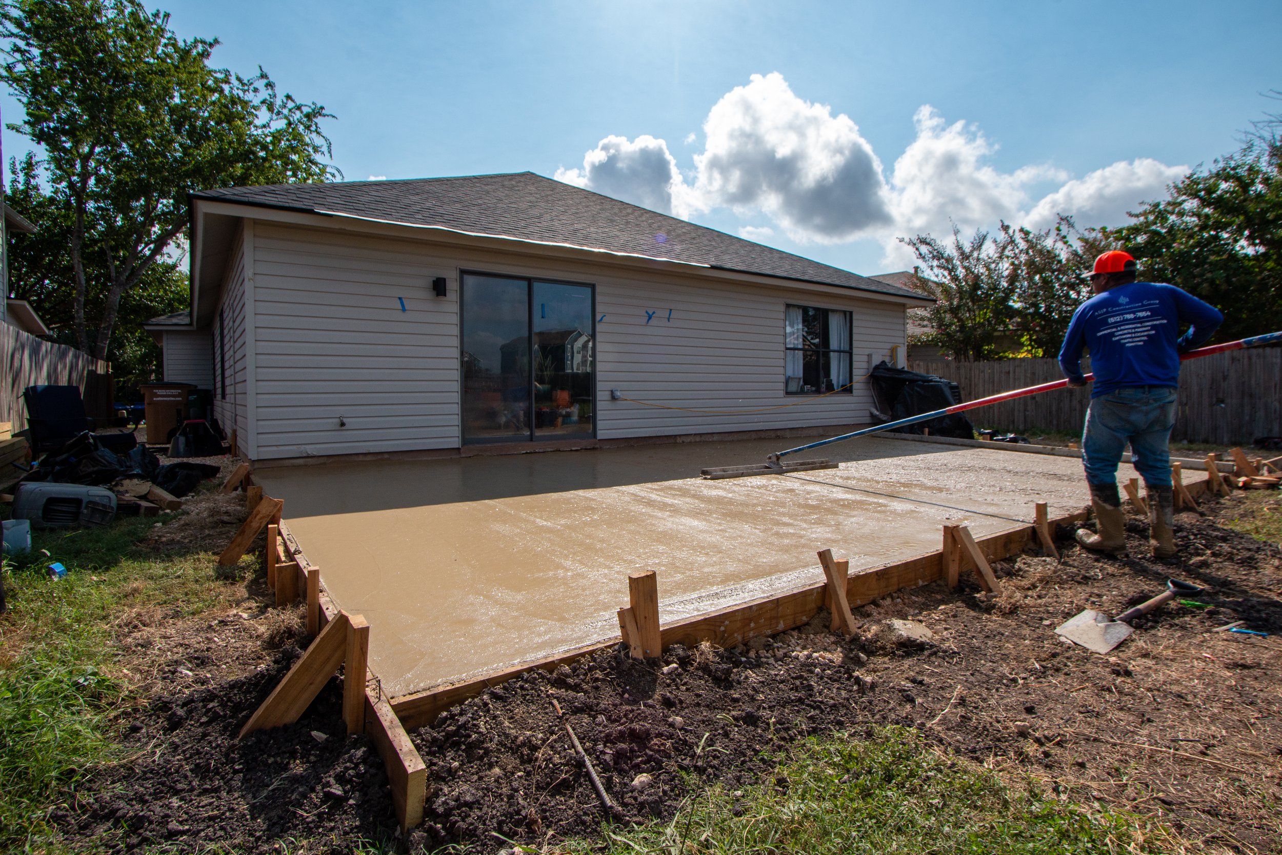 Construction worker smoothing wet concrete for a backyard patio or driveway in a residential area on a sunny day.