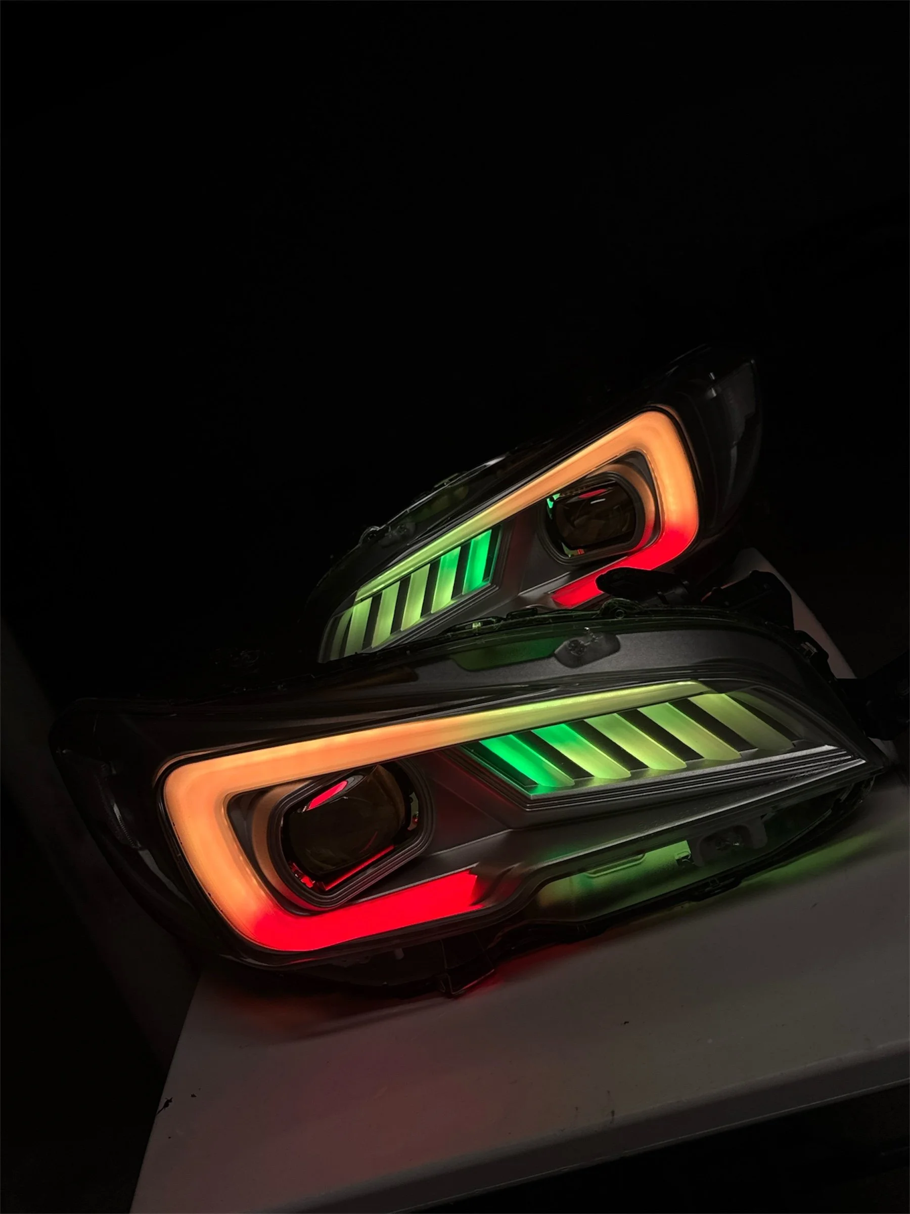 Close-up of a car's headlight with colorful LED lights in a dark environment.