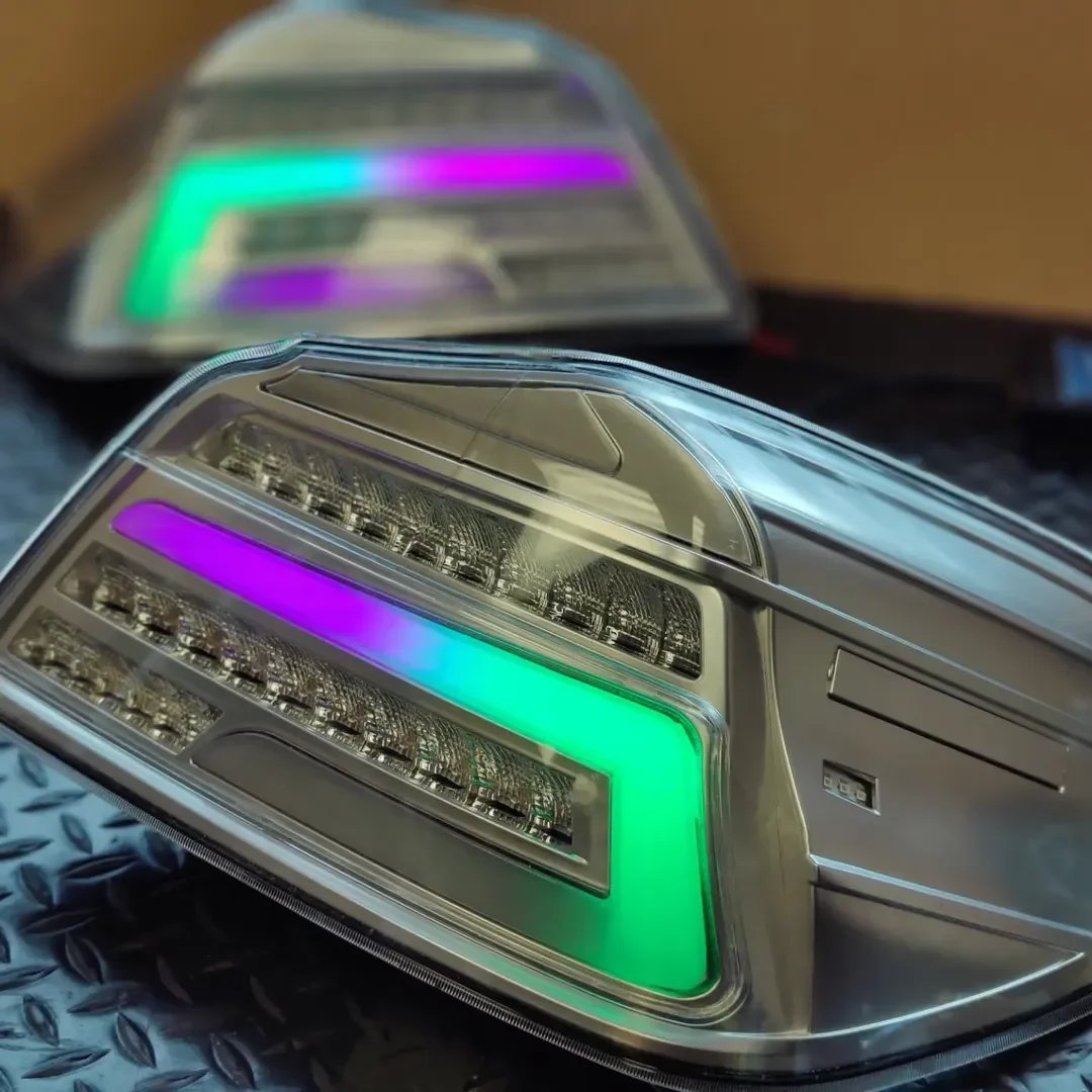 Close-up of modern car headlights with colorful LED lights, one headlight in focus with the other blurred in the background.