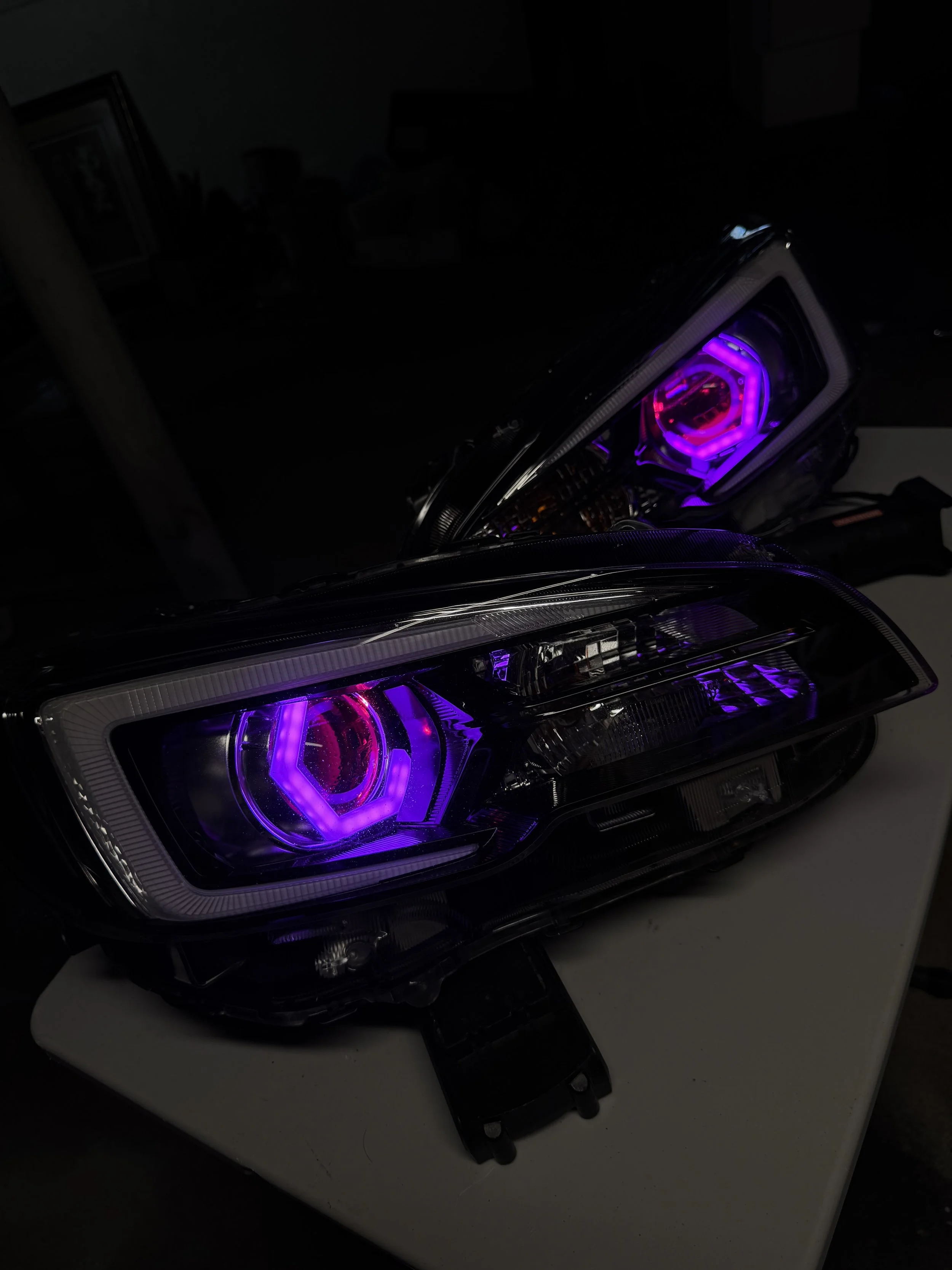 Car headlights with purple and pink LED lights on a white surface.