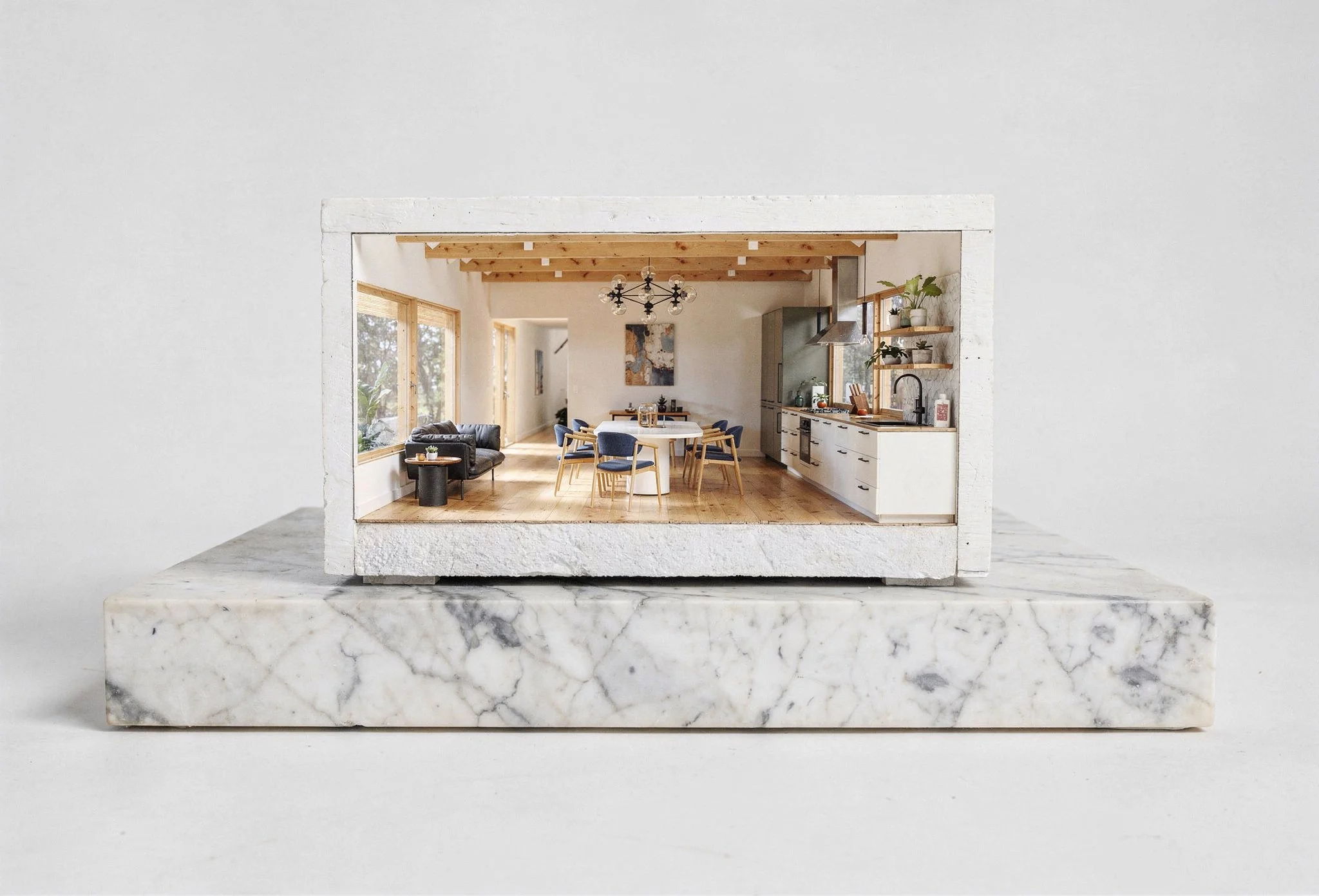 A miniature model of a modern kitchen and dining area inside a white stone frame displayed on a marble block.