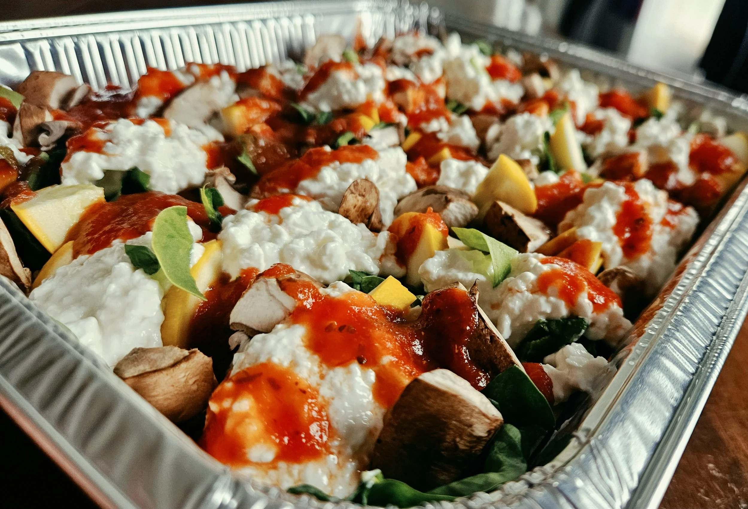 A tray of baked chicken topped with tomato sauce and cheese, garnished with chopped green herbs and served with seasoned roasted potatoes.