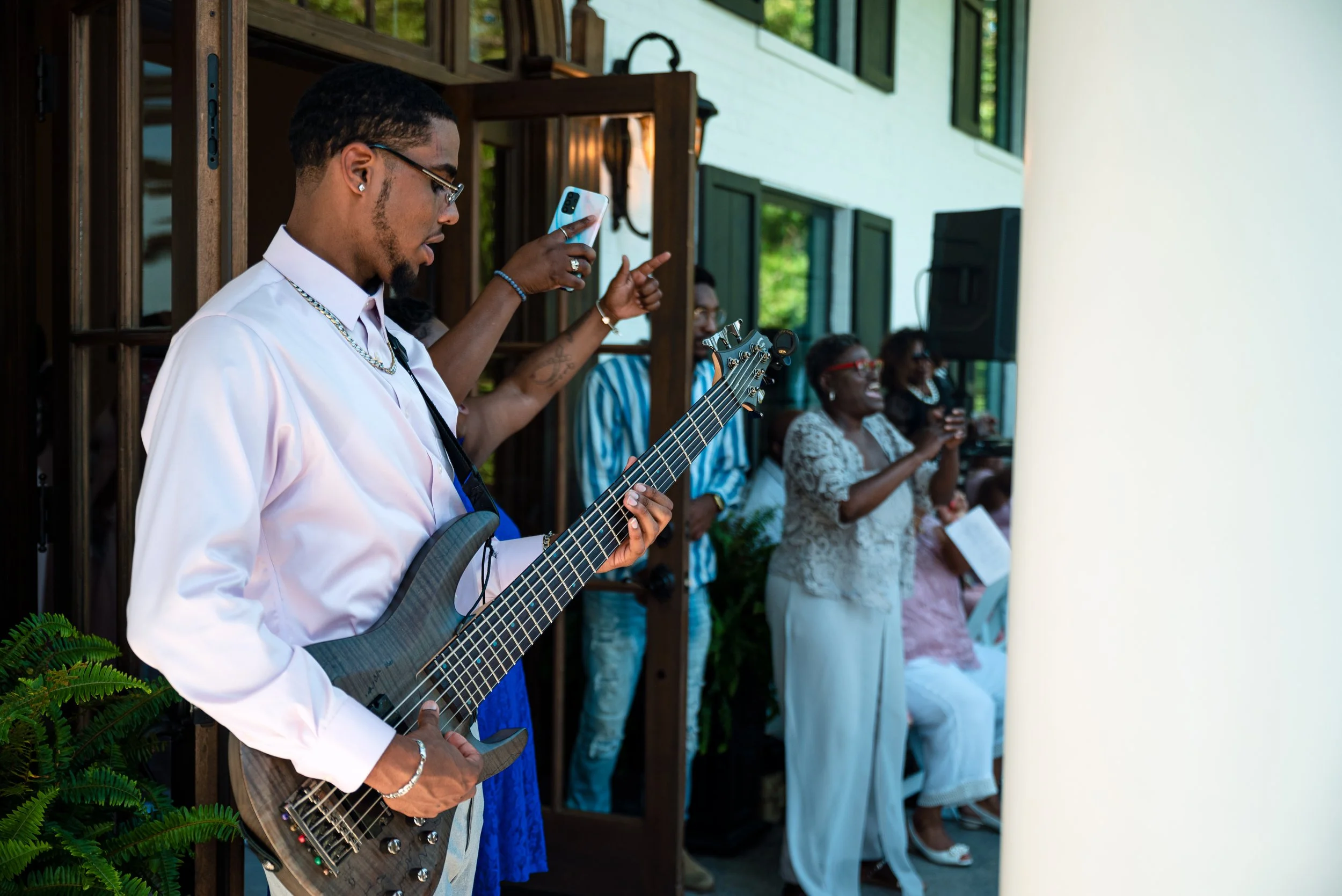 A man playing an electric guitar at an outdoor gathering with people singing and clapping in the background.