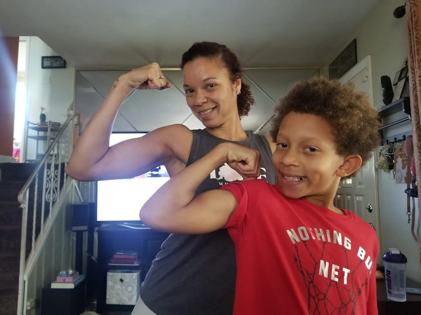 A woman and a young boy flexing their biceps and smiling in a living room.